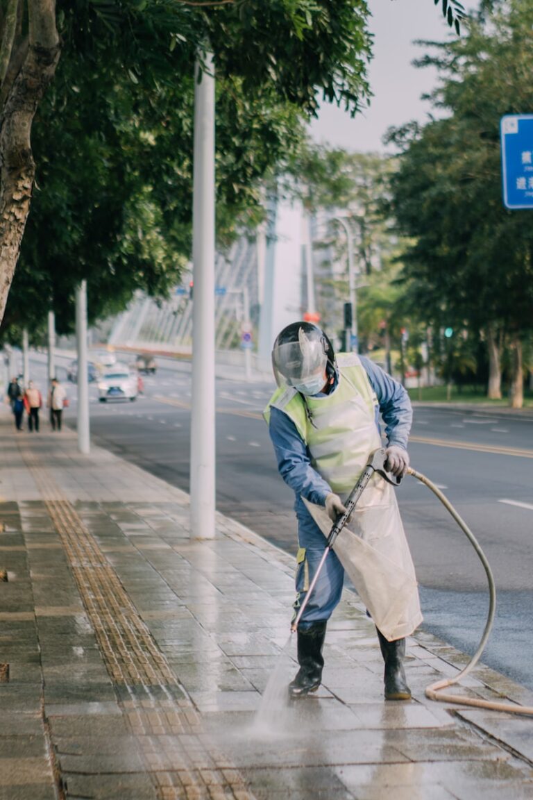 a man in a yellow vest is spraying water on a sidewalk
